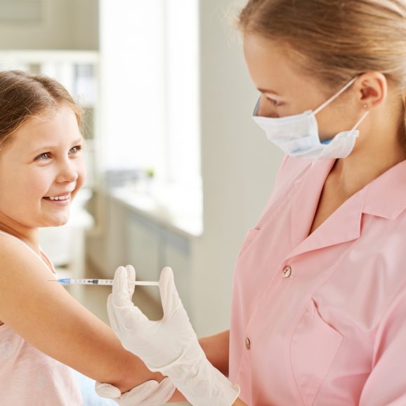 Adorable girl looking at nurse while she making her an injection in clinics